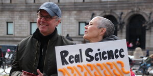 Zwei Demonstranten, einer hält ein Schild, auf dem „Real Science, Fake President“ steht