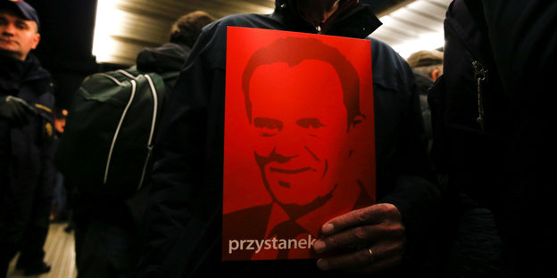 Am Warschauer Zentralbahnhof hält jemand ein rotes Plakat mit dem Gesicht von EU-Ratspräsident Donald Tusk vor der Brust, um ihn zu begrüßen.