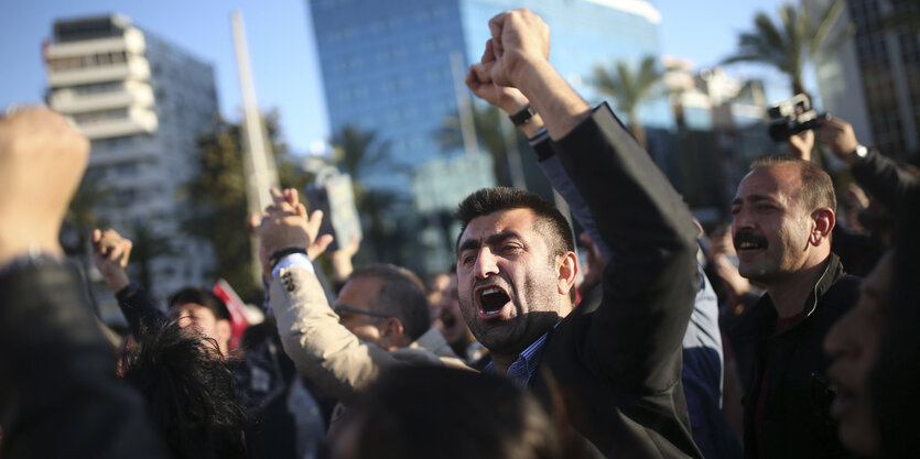 Ein wütender türkischer Demonstrant hat kämpferisch die linke Faust geballt, hinter ihm weitere Demonstranten