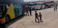 Zwei kleine Kinder gehen Hand in Hand über einen Platz in Richtung eines Busses