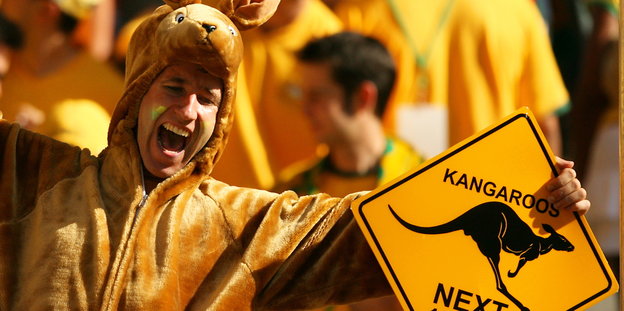 Ein Mann in einem Känguru-Kostüm hält ein Schild, das vor Kängurus warnt, hoch
