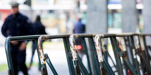 Drei Passanten, einer von ihnen Polizist, sind im Hintergrund verschwommen zu erkennen, vorne stapeln sich die vorbereiteten Absperrgitter