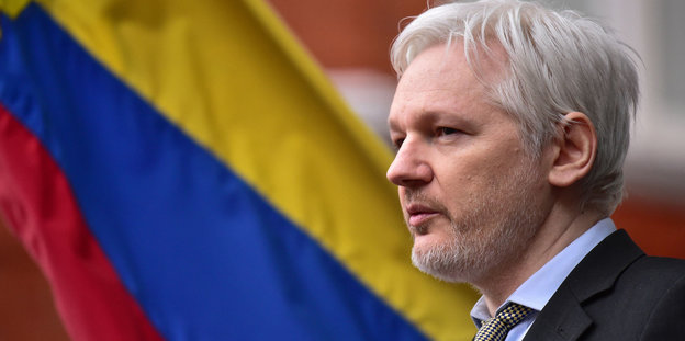 Julian Assange im Profil vor einer ecuadorianischen Flagge