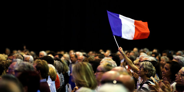Sitzende Menschen blicken in dieselbe Richtung, eine französische Flagge weht mittendrin