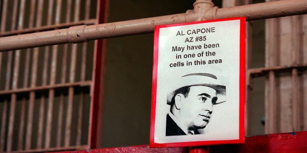 An einem Stahlrohr hängt ein Schild, auf dem steht „Al Capone may have been in one of the cells in this area“, dahinter Gitterstangen