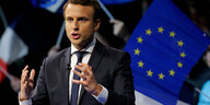 Emmanuel Macron gestikuliert, während er eine Rede hält, im Hintergrund werden Frankreich und Europa-Flaggen geschwenkt