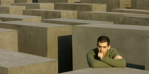 Der Schriftsteller Ori Ginat stützt sieine Arme nachdenklich auf eine der Stelen im Berliner Holocaust-Mahnmal