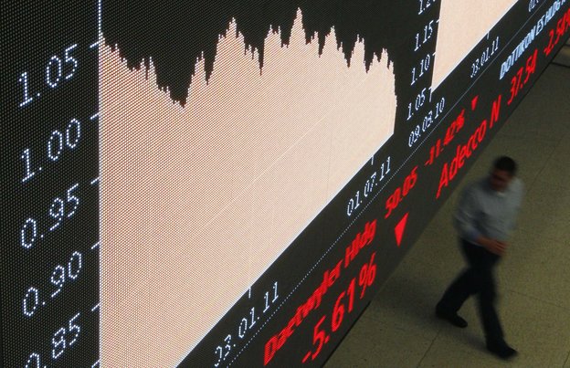 Eine Anzeigentafel in der Börse zeigt fallende Kurse, im Hintergrund läuft ein Mann vorbei