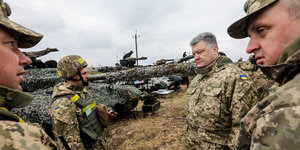 Petro Poroschenko steht neben Soldaten, sie alle tragen Uniformen, hinter ihnen stehen Panzer