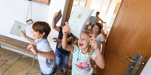 Kinder rennen aus einem Klassenzimmer. Sie halten Zeugnisse in der Hand