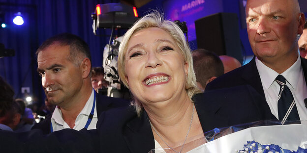 Marine Le Pen lächelt, umrahmt von zwei Sicherheitsleuten