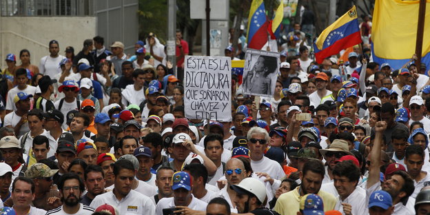 Eine Gruppe von Demonstranten mit Fahnen Venezuelas, in der Mitte ein Schild mit der Aufschrift "Das ist die Diktatur von der Chavez und Fidel träumten" auf Spanisch.