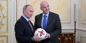 Zwei Männer in Anzügen halten gemeinsam einen Fußball in den Händen