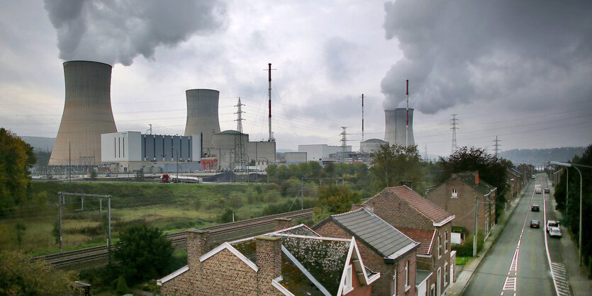 Im Hintergrund Kühltürme eines AKW mit großen Dampfwolken. Im Vordergrund ein paar Häuser und eine Straße.