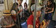 Zahlreiche asiatisch aussehende Menschen in einer Bahn, die alle auf ihre Smartphones schauen