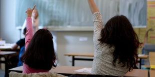 Zwei Mädchen mit dunklen Haaren melden sich in einer Schulstunde