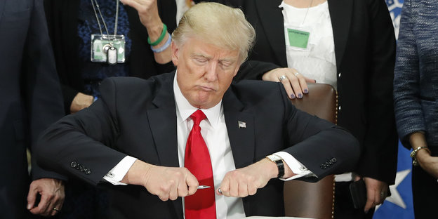 Donald Trump zieht mit beiden Händen an einem Kuli
