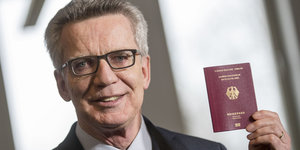 Ein Mann mit Brille hält lächelnd seinen deutschen Pass in die Höhe