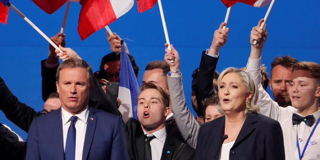 Nicolas Dupont-Aignan (l) neben Marine Le Pen, dahinter Menschen, die französische Fahnen schwenken