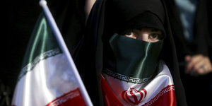 Eine Frau mit Kopftuch hat sich eine iranische Flagge vor den Mund gebunden