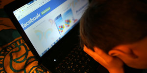 ein Junge hat auf seinem Laptop Facebook geöffnet und reibt sich die Augen