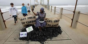 Aktivistin auf einem Kohlehaufen auf einer Seebrücke, zwei Säcke tragen die Aufschrift: "Let them eat carbon“