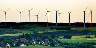 Ein Dorf am Berghang, darüber Windräder