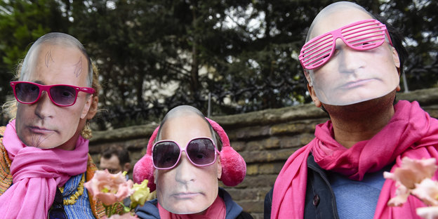Drei rosa vermummte Männer mit Putin-Masken