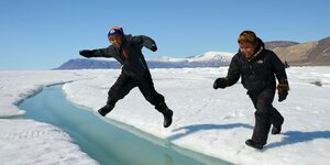 Zwei Jungs springen über einen kleinen Fluss im Eis
