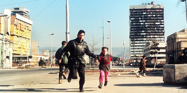 Ein Mann mit einem kleinen Mädchen an der Hand rennt auf der Flucht vor Heckenschützen durch Sarajevo