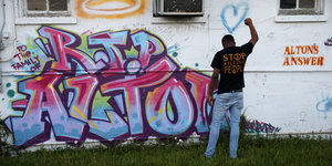 Ein schwarzer Mann hebt die rechte Faust vor einem Graffiti
