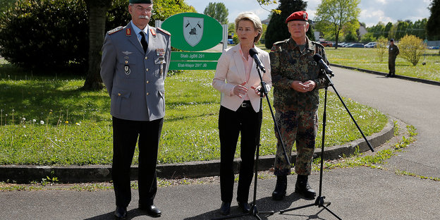 Verteidigungsministerin gerahmt von zwei Soldaten vor einem Mikro im Freien