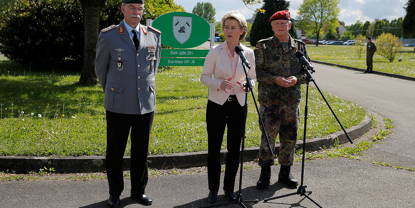 Verteidigungsministerin gerahmt von zwei Soldaten vor einem Mikro im Freien