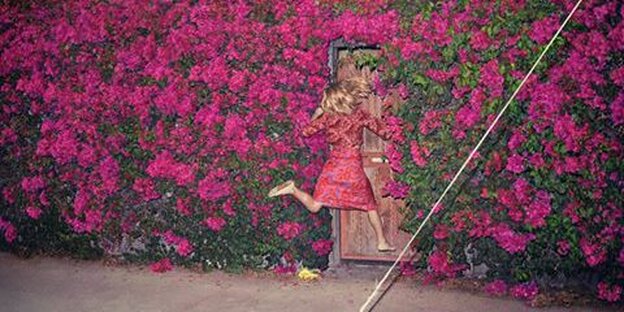 Eine Frau rennt gegen eine Tür. Die Wand ist von roten Blumen berankt.