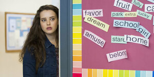 Hannah Baker, gespielt von Katherine Langford, steht neben einer Pinnwand in der Schule