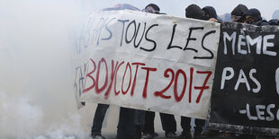 Demonstranten halten, eingehüllt in Rauch, ein Banner in die Höhe, auf dem "Boycott 2017" zu erkennen ist