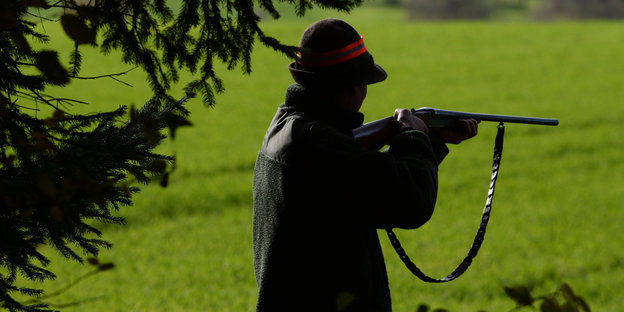 Ein Jäger steht während einer Treibjagd mit seinem Gewehr schussbereit am Waldrand.