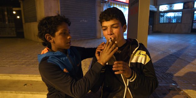 Ein Junge in Trainingsjacke lässt seinen Kumpel an einer Zigarette ziehen