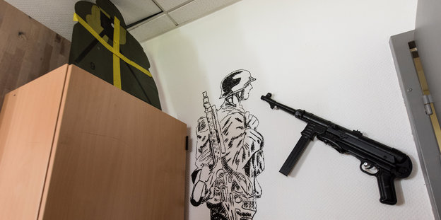 Links ein Schrank, daneben ein an die Wand gezeichneter Soldat und eine Maschinenpistole.