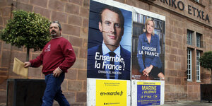 Zwei Wahlplakate mit den Konterfeis Macrons und Le Pens hängen nebeneinander, dahinter geht ein Mann