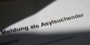 Auf einem Blatt steht der Schriftzug "Meldung als Asylsuchender"