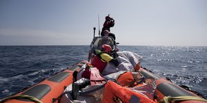 Drei Menschen sitzen in einem Boot mit Rettungswesten auf offenem Meer