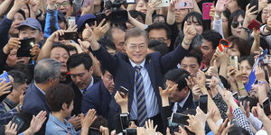 Kandidat Moon Jae In steht inmitten einer Menschenmenge und hebt beide Hände, die Daumen in die Höhe gestreckt