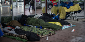 Menschen liegen in Schlafsäcke gehüllt vor einem Schaufenster