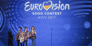 Eine Band bestehend aus drei jungen Männern vor einem blauen Hintergrund mit der Aufschrift "Eurovision Song Contest Kiev 2017"