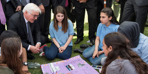 Frank-Walter Steinmeier sitzt zwischen Jugendlichen vor einem bunten Plakat das zwischen ihnen liegt