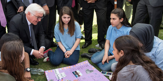 Frank-Walter Steinmeier sitzt zwischen Jugendlichen vor einem bunten Plakat das zwischen ihnen liegt