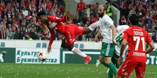 Ein Fußballspieler fliegt waagerecht durch die Luft, vor ihm ein Fußball, neben ihm mehrere Fußballspieler