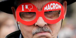 Ein Mann trägt eine rote Pappbrille, auf der ein Dislike-Symbol und Macron zu sehen sind