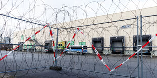 ein Absperrgitter mit Stacheldraht auf dem Parkplatz eines Logistikunternehemens